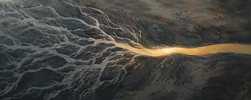 Aerial view of braided silver river channels flowing across dark stone into a single golden river